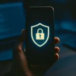 Una mano che tiene uno smartphone con un icona di lucchetto o scudo sullo schermo