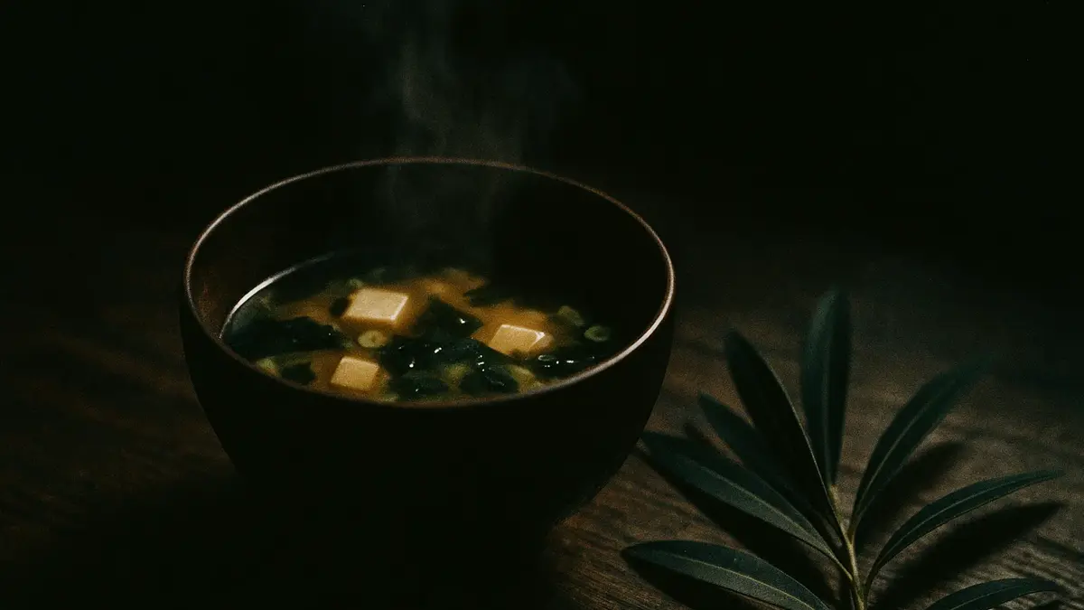Ciotola di zuppa di miso su un tavolo con foglie verdi accanto